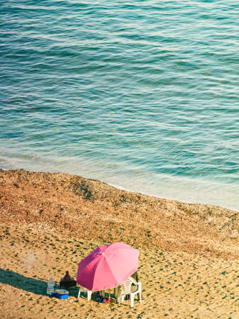 Picnic on beach sea shore. Pink umbrella and chairs on seashore. View from above.の写真素材