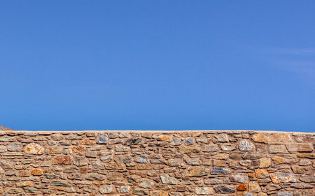 Symmetrical shot, wall made of old stones rocks and clear blue sky with copy space.