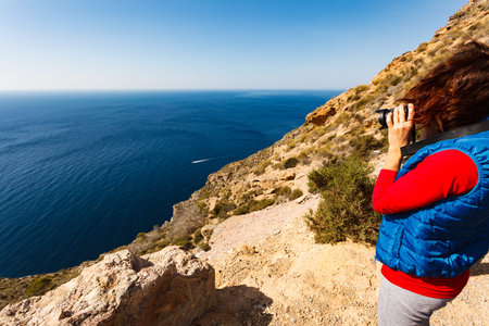 Tourist adult woman with camera taking travel photo from seacsape in Spain.