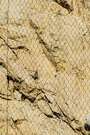 Grunge wall stone or solid nature rock with net for protection from landslide sliding down rocks from mountain or cliff.の写真素材