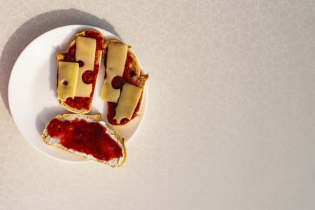 Preparing breakfast meal. Bread slices with butter, jam and cheese on white plate.