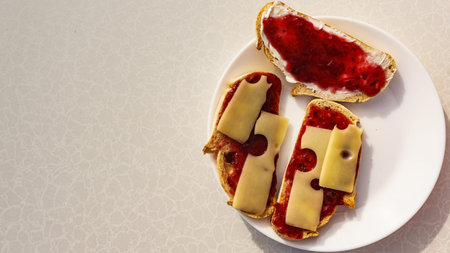 Preparing breakfast meal. Bread slices with butter, jam and cheese on white plate.