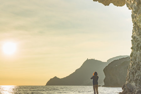 Tourist woman with camera taking travel photo on Monsul beach at sunset. Cabo de Gata Nijar Natural...
