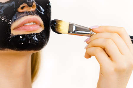 Young woman applying with brush black detox peel off mask to her face. Girl taking care of skin. Beauty treatment. Skincare.の写真素材