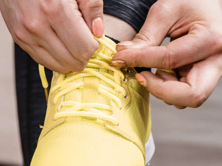 Woman in sportswear sitting on sofa indoor getting ready for exercises. Tying up shoesの写真素材