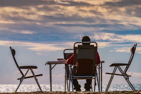 Male tourist person sitting on beach seashore at sunset, relaxing and enjoying scenic sea view. Summer holidays.の写真素材