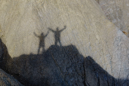 Shadow of two people on rock during hiking in stone mountains. Couple holdings hands, arms raised. Happiness and freedom.の写真素材
