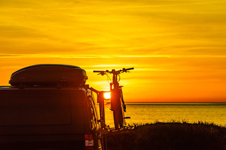 Camper, recreational vehicle with bicycles on rack camping on beach at sunrise. Holidays and travel...