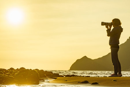 Tourist woman with camera take travel picture on Monsul beach at sunset. Cabo de Gata Nijar Natural...