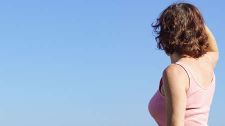 Female person against blue sky looking at horizon enjoying fresh airの写真素材