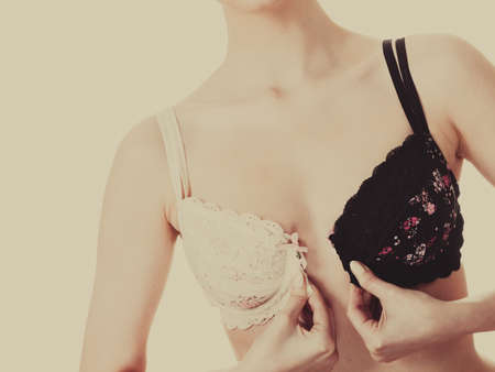Female dilemmas - black or white underwear. Woman trying to choose perfect bra. Girl of smoothy glorious body with brassiere dilemma. Toned imageの写真素材
