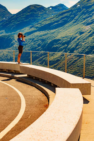 Female tourist with camera taking travel picture, enjoying mountains landscape from Ornesvingen viewing platform, Norway.の写真素材