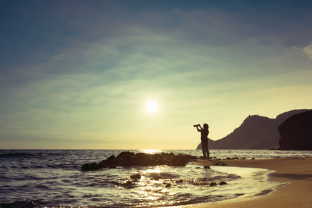Tourist woman with camera taking travel picture on Monsul beach. Cabo de Gata Nijar Natural Park,...