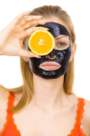 Woman with carbo detox black peel-off mask on face holding orange fruit. Teen girl taking care of oily skin, cleaning the pores. Beauty treatment. Skincare.の写真素材