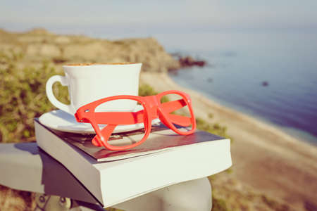Reading on holidays. Coffee cup and book on chair outdoors against blue sea water background.の写真素材