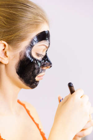 Young woman applying with brush black detox mud mask to her face. Girl taking care of skin. Spa treatment. Skincare. Side viewの写真素材