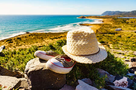 Hat and shoes, summer walking equipment on mediterranean sea coast. Murcia region, Calblanque Regional Park in Spain. Hiking, camping, active lifestyle.の写真素材