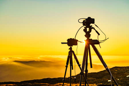Camera on tripod take photo from burning sunset above clouds.の写真素材