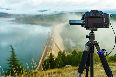 Camera on tripod take travel picture from morning fog over dam on Embalse de Aguilar de Campoo in...