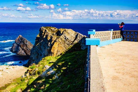 Woman with camera take travel photo from seascape of Atlantic ocean and Asturias rocky coast at Cape Penas. Sea shore with high cliffs in north Spain.の写真素材