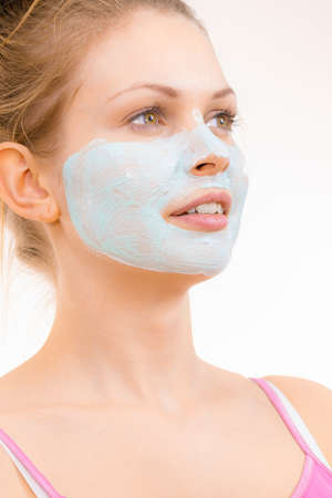 Young woman applying green mud mask to face, on white. Teen girl taking care of oily skin, purifying the pores. Beauty treatment. Skincare.の写真素材