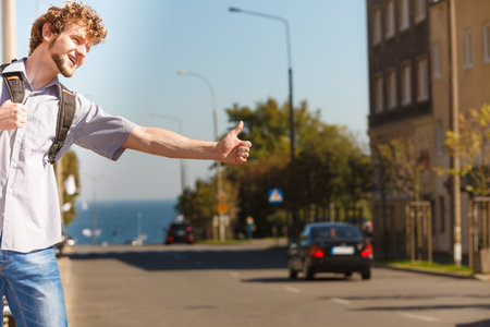 Young man hitchhiking on summer vacation. Happy guy tourist beside road with thumb up gesture having fun.の写真素材