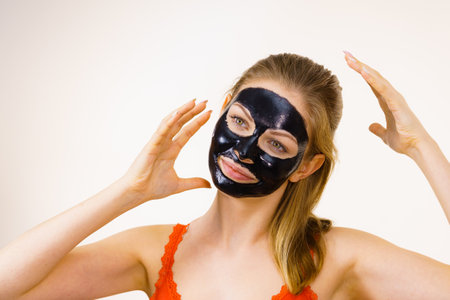 Young woman with carbo detox black peel-off mask on her face, on white. Teen girl taking care of oily skin, cleaning the pores. beauty treatment. skincare.の写真素材