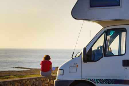 Woman traveling with motor home, relaxing outdoors with book, enjoy fresh air on sea coast. Reading on holidays. relax time. Caravan holiday.の写真素材