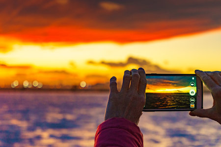 Woman hand photographing seascape at sunset with mobile phone.の写真素材