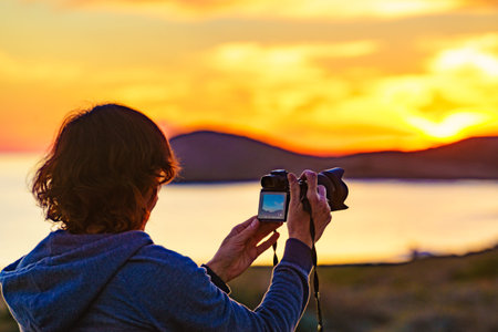 Tourist woman with camera taking travel photo on nature at sunset time.