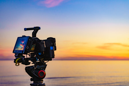 Professional camera on tripod taking picture film video of sunset over sea.の写真素材
