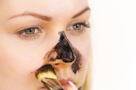 Young woman being apply with brush purifying charcoal mask, black cosmetic to her face. Female taking care of oily skin. Beauty treatment. Skincare.の写真素材