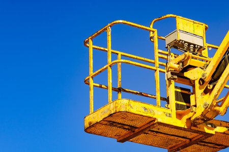 Basket lift, yellow lifting platform on construction site against blue sky. Industrial machine, work...