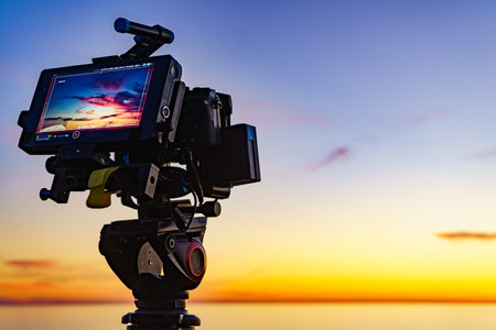 Professional camera on tripod taking picture film video of sunset over sea.