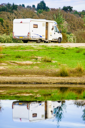 Camping on nature. Camper vehicle at lake shore reflecting in water. Povoa e Meadas Dam in Castelo de Vide, Alentejo Portugal. Travel in motor home.の写真素材
