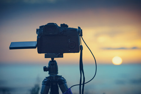 Professional camera on tripod taking travel photos film video of sunrise over sea. Photography.