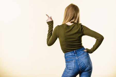 Back view of woman with blonde hair on white background showing something, pointing with finger at copy space.の写真素材