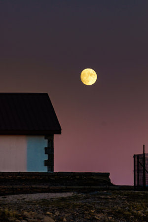 Full moon at night on dark sky above house building. Moonlight.の写真素材