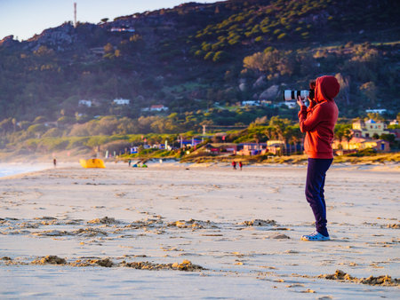 Tourist woman with camera take travel picture on Tarifa beach. Costa de la Luz, province of Cadiz, Andalusia in Spain.の写真素材