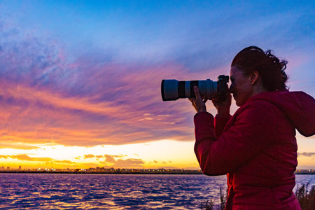Woman photographing seascape at sunset with professional camera.