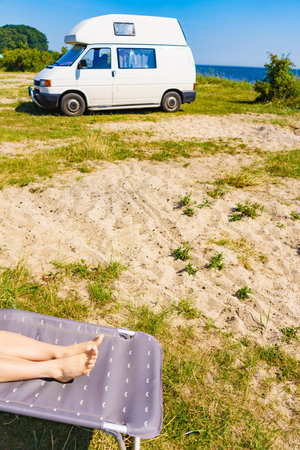 Woman feet on deck chair. Female relaxing enjoying sun on sunny summer day in front of rv campervan..の写真素材