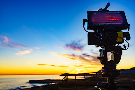 Professional camera on tripod taking picture film video of sunset over sea.の写真素材