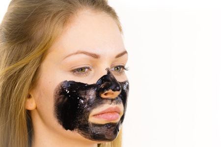 Young woman applying carbo detox black mask to her face. Teen girl taking care of oily skin, cleaning the pores. Spa treatment. Skincare.の写真素材