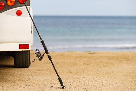 Camper vehicle and fishing rod on sand beach. Camping on sea shore. Activity on holidays.の写真素材