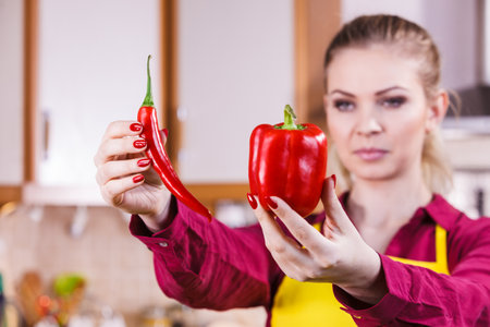 Woman comparing bell pepper and red hot chili. Vegetables, spices, food concept.の写真素材