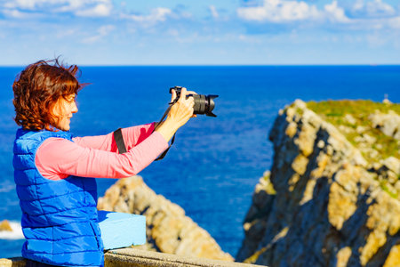 Woman with camera take travel picture from sea landscape, Atlantic ocean and Asturias coast at Cape Penas in north Spain.の写真素材