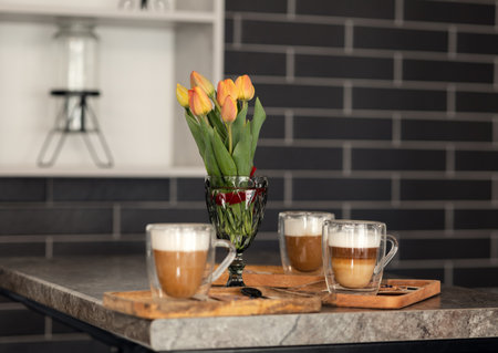 a bouquet of orange-red tulips and a cup of hot coffee are on the tableの写真素材
