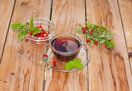 Cup of tea with leaves and berries ripe strawberry on a wooden background.の写真素材