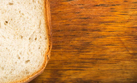 Slice of Bread on an Old Cutting Board Background. Porous and Wooden Texture Closeupの写真素材