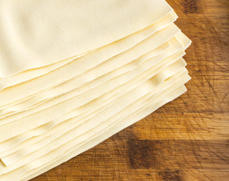 Heap of Uncooked Lasagna Sheets or Dry Italian Pasta on Old Wooden Cutting Boardの写真素材